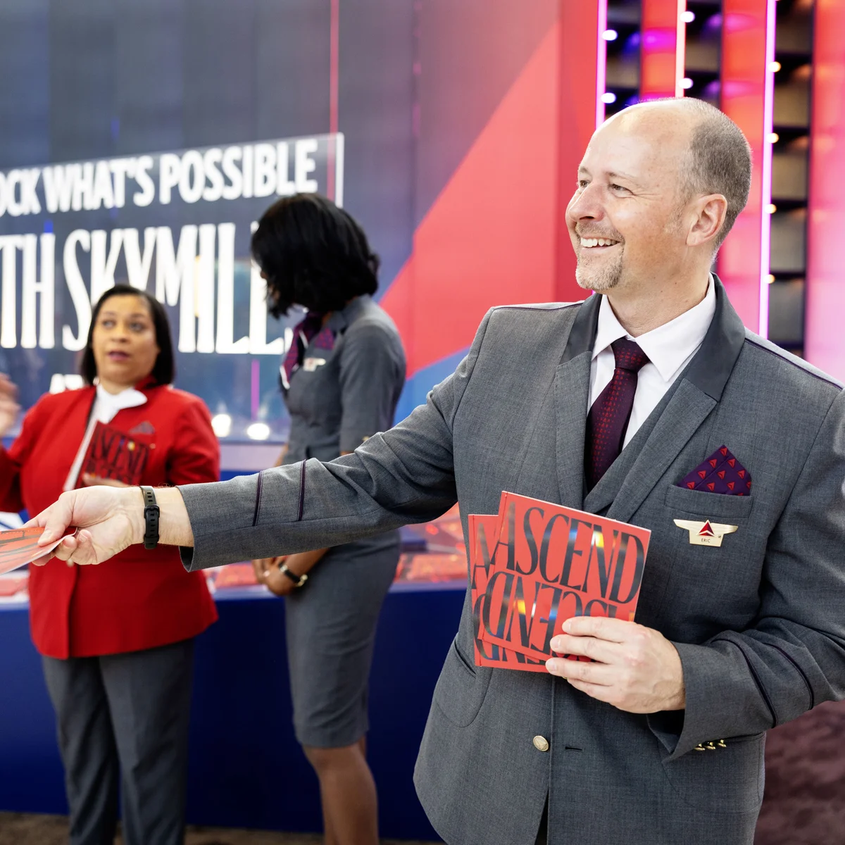 Austin-based Delta Air Lines flight attendant cheerfully welcomes visitors to SXSW 2024 at Austin-Bergstrom International Airport, with an invitation to grab a copy of Delta's curated guide to navigating SXSW 2024.