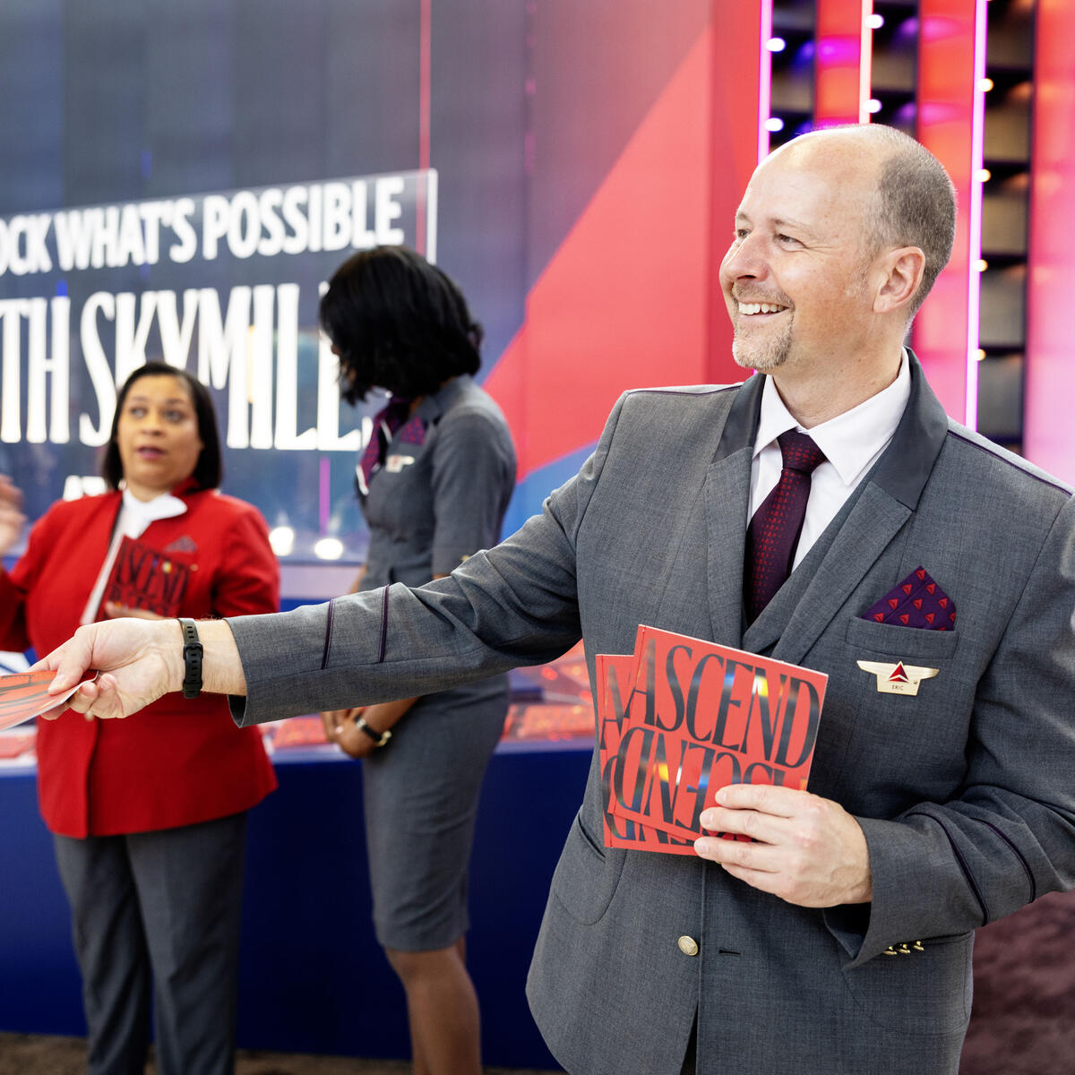 Austin-based Delta Air Lines flight attendant cheerfully welcomes visitors to SXSW 2024 at Austin-Bergstrom International Airport, with an invitation to grab a copy of Delta's curated guide to navigating SXSW 2024.