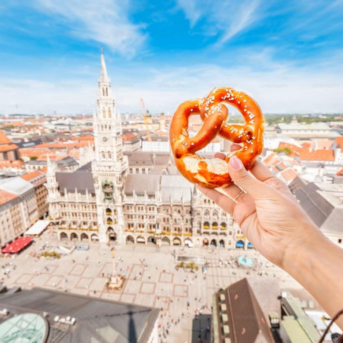 A tourist's hand holds a German pretzel against the backdrop of the city of Munich.