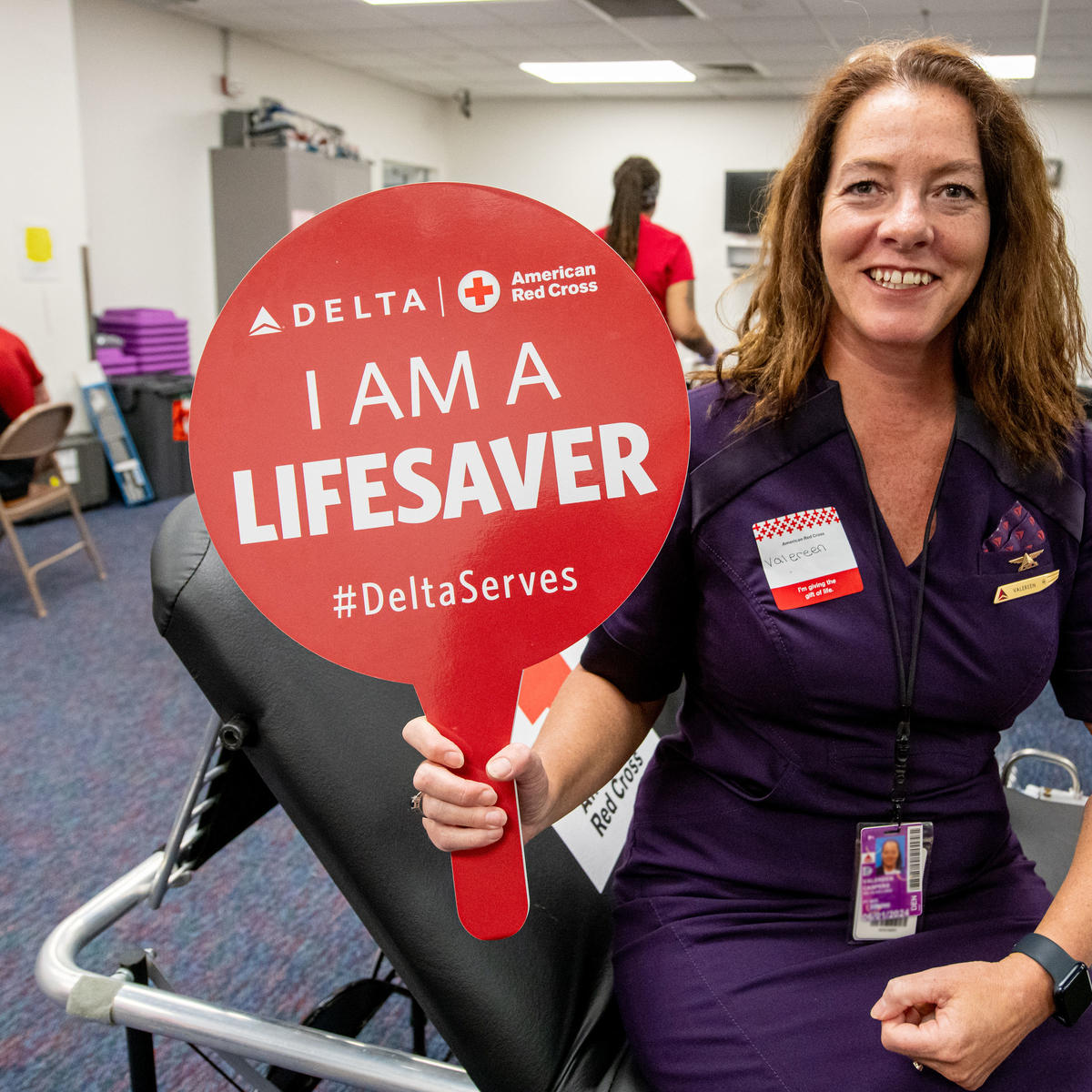 A Delta employee holds up a sign that says "I am a lifesaver" while giving blood.