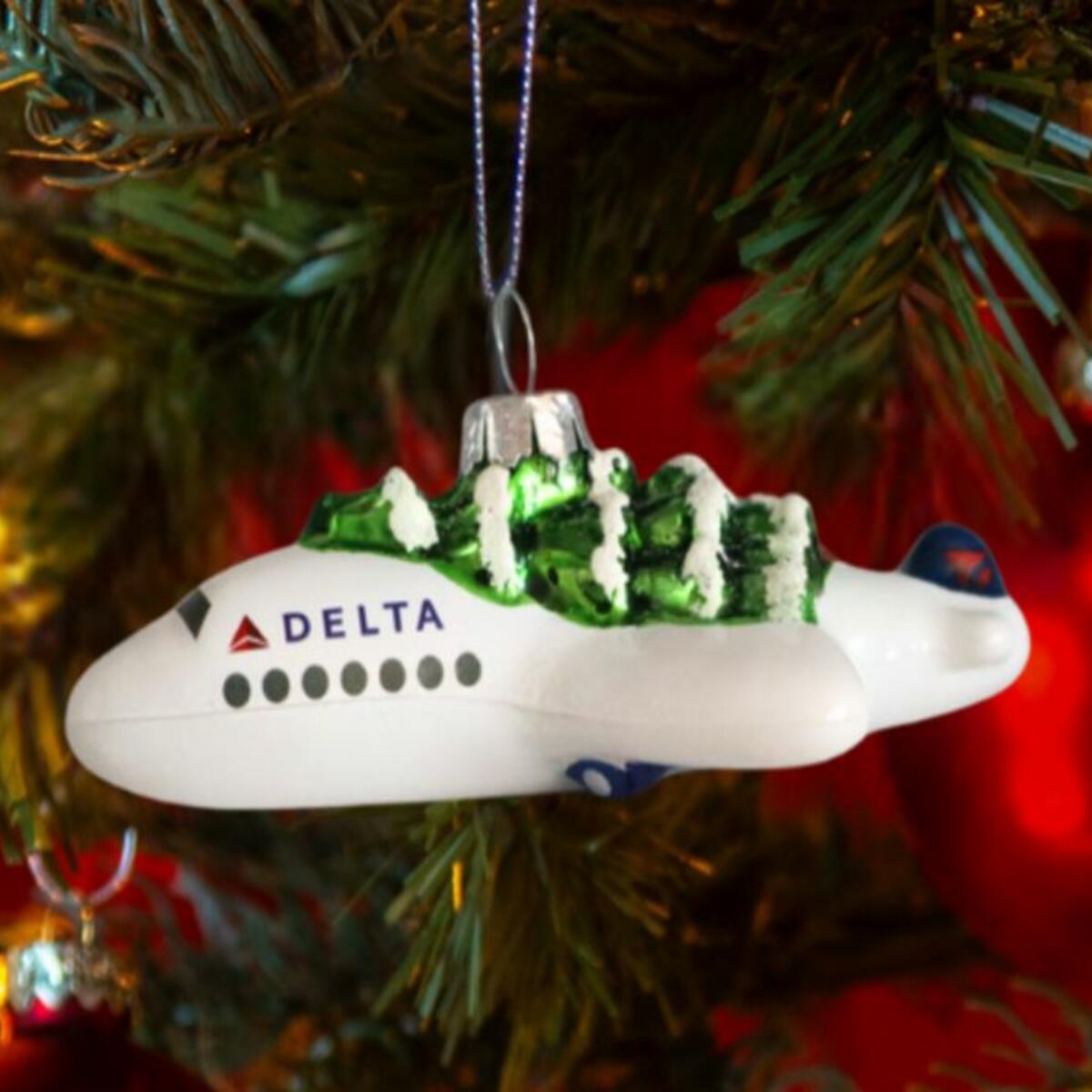 Soar into style with our Festive Delta Plane Ornament. Made of glass with a whimsical tree on top, make sure to snag one before it takes off! 
