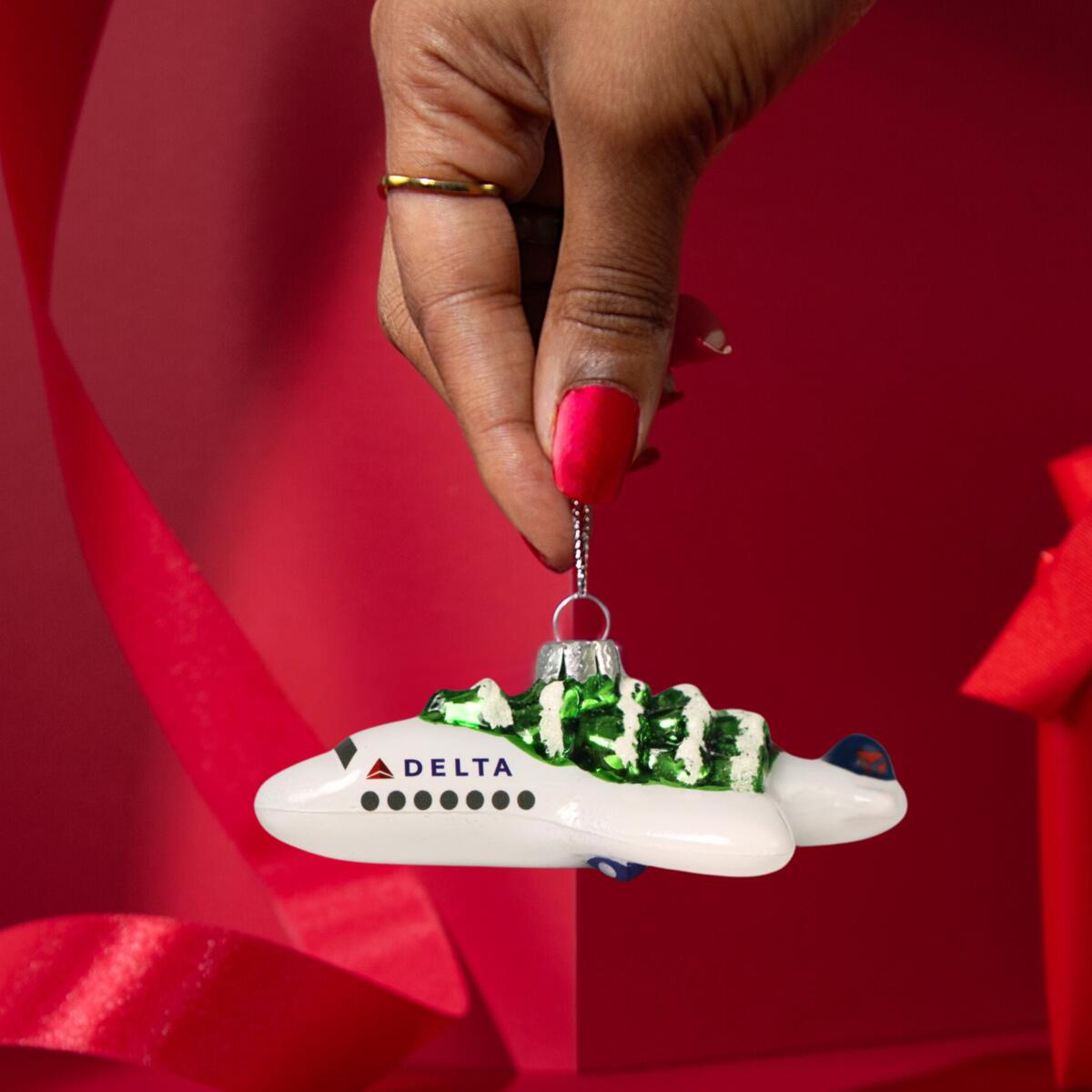 Soar into style with our Festive Delta Plane Ornament. Made of glass with a whimsical tree on top, make sure to snag one before it takes off! 