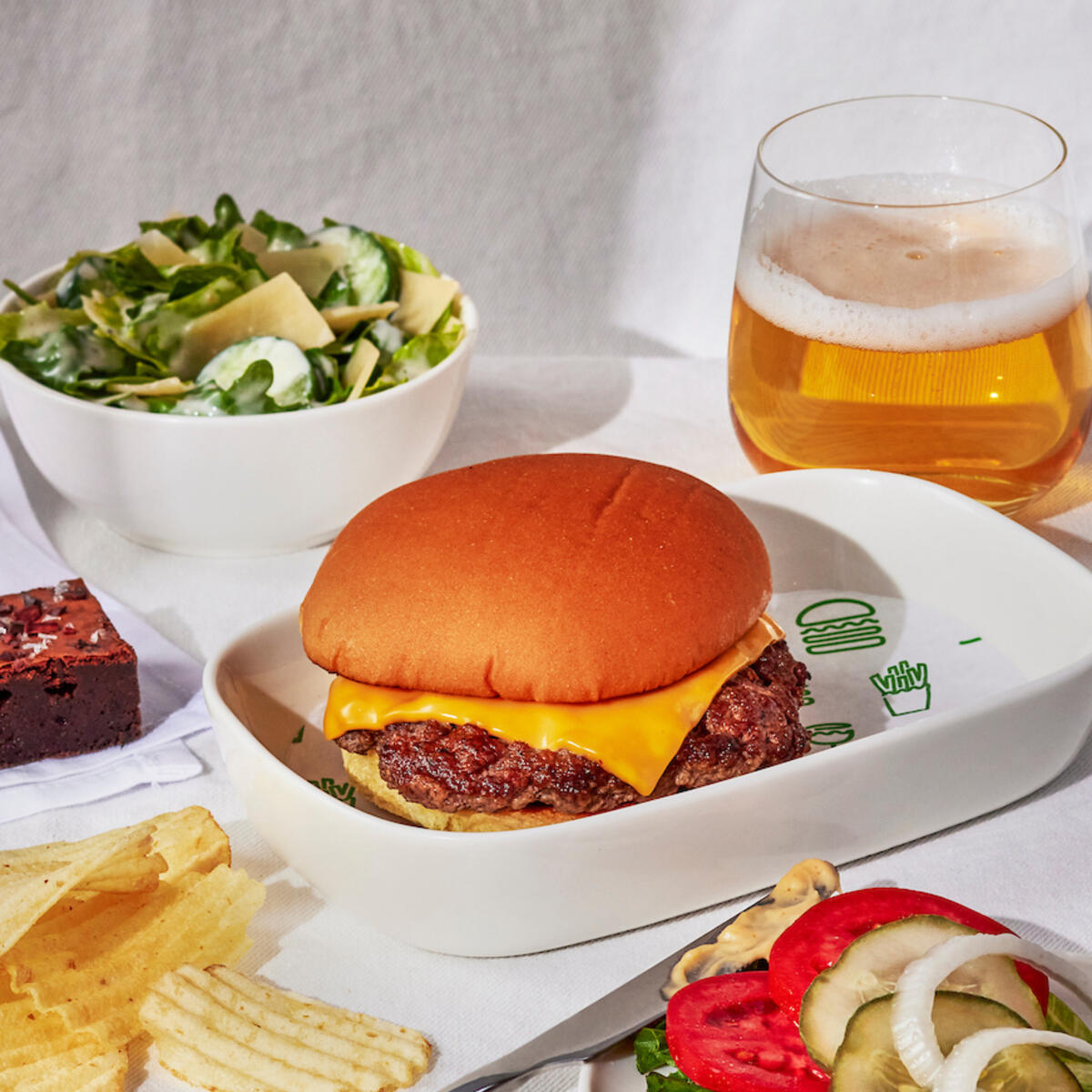 A Shake Shack burger with a side of chips, a salad, and burger fixings.