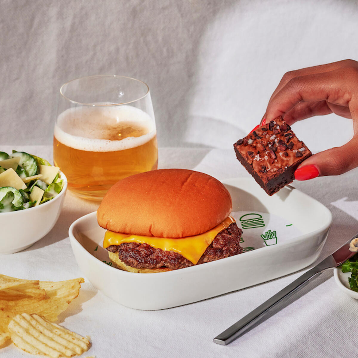 A Shake Shack burger with a side of chips, a salad, and burger fixings.