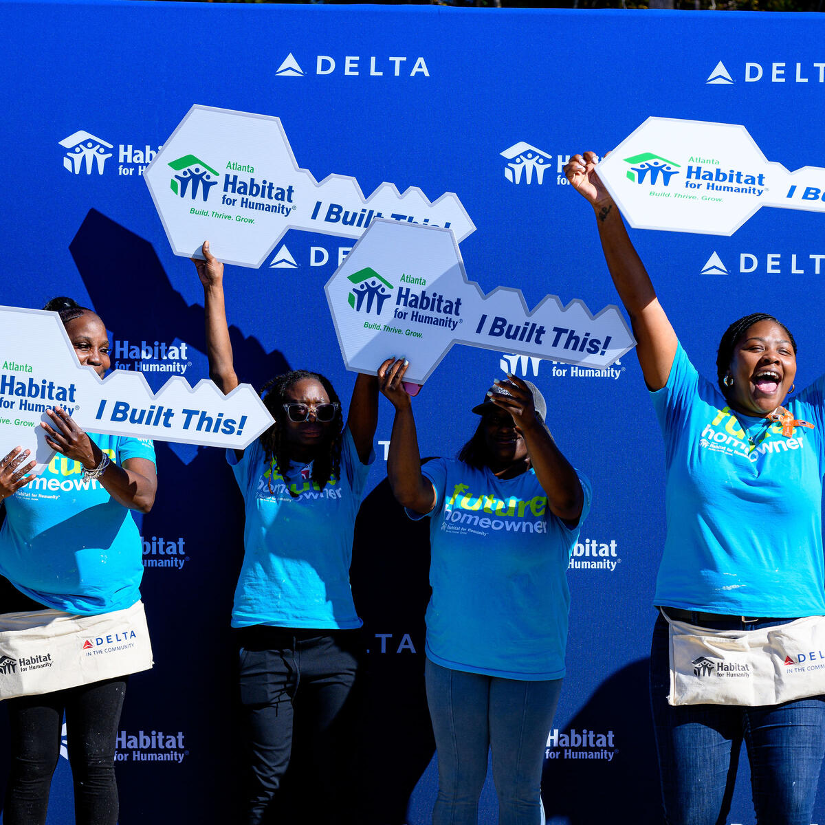 Habitat for Humanity homeowners pose for a photo cheering and holding large key-shaped cutouts.