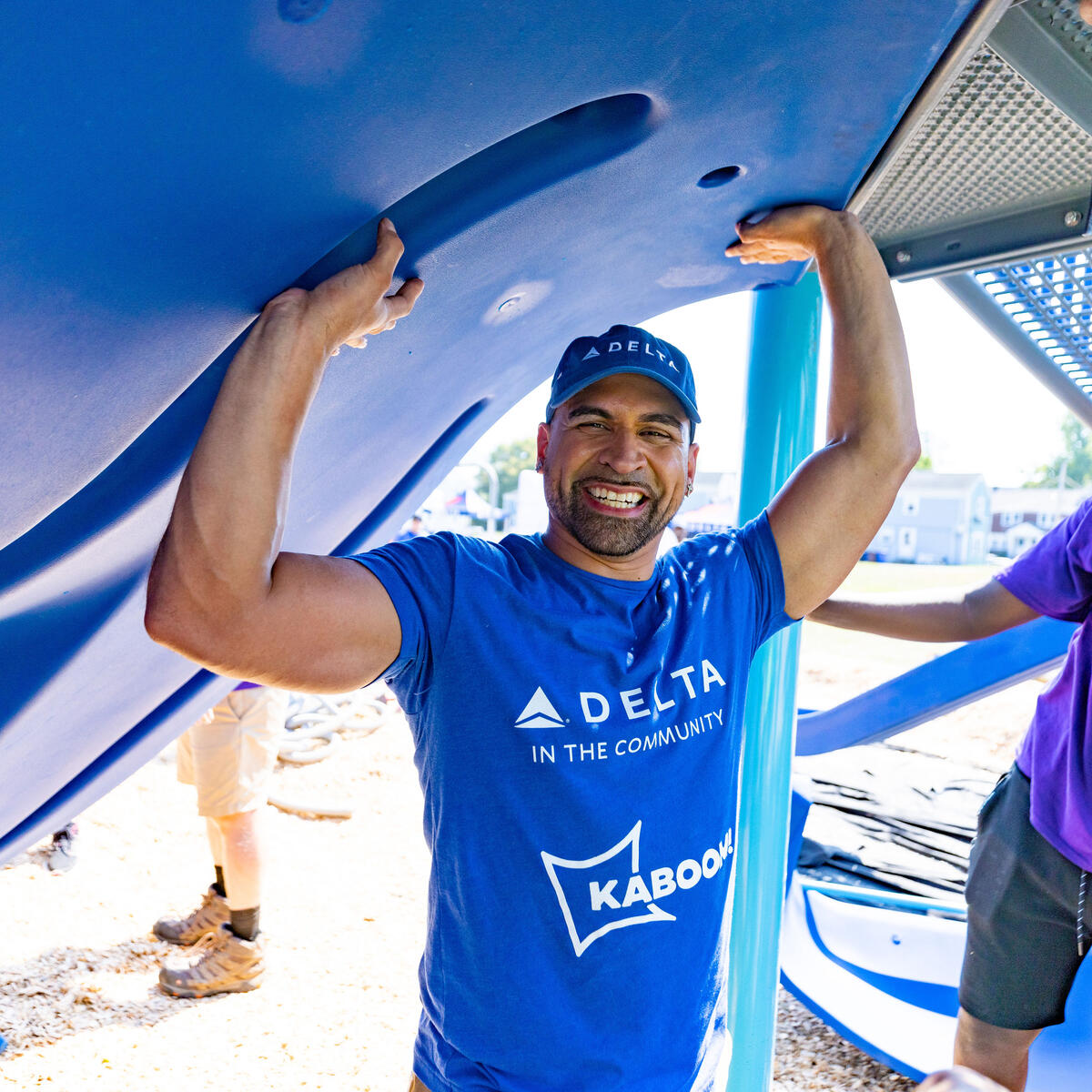 Delta employee volunteer smiling as he holds up a blue playground piece at a Kaboom build