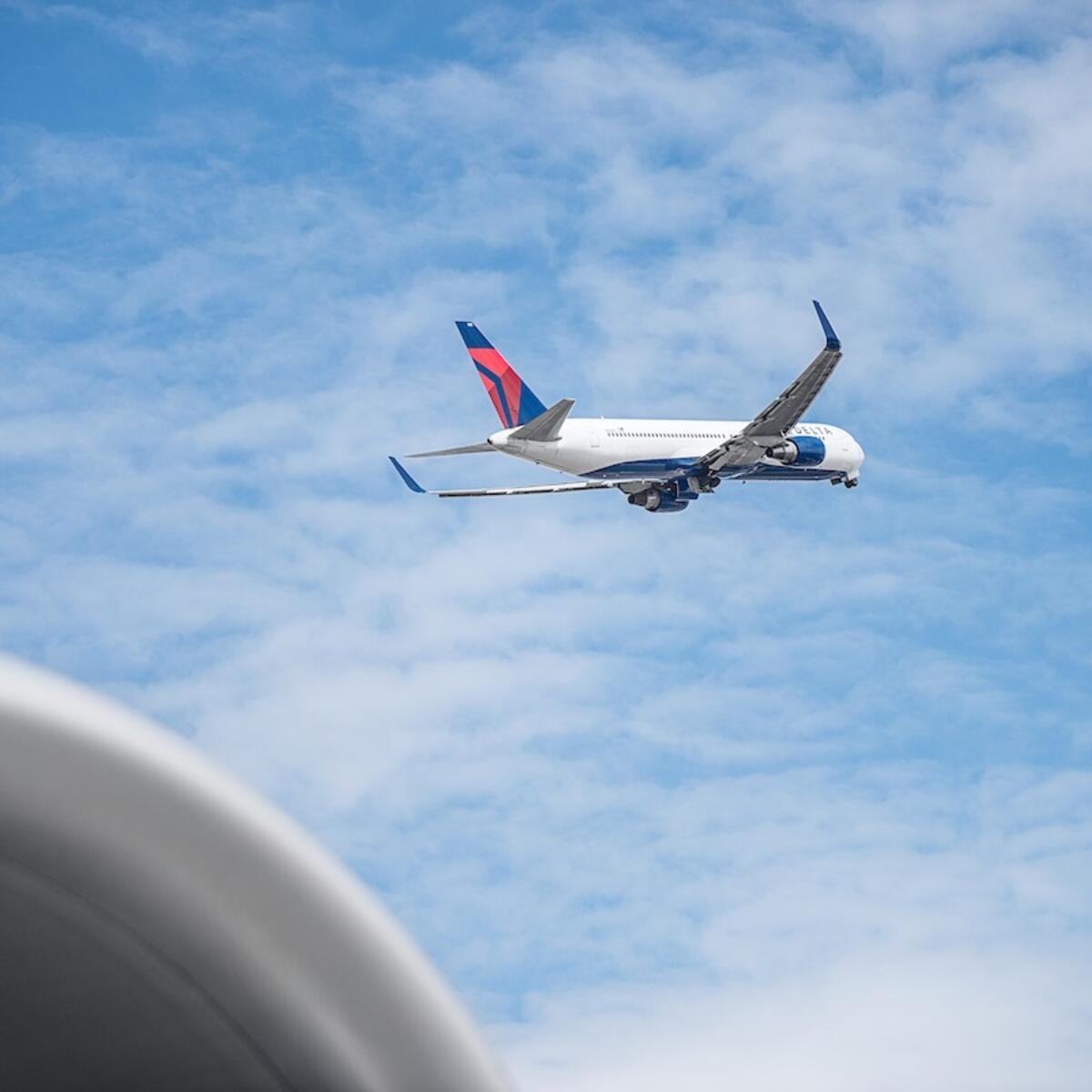 Delta 767 aircraft shortly after takeoff with blue sky and clouds in background