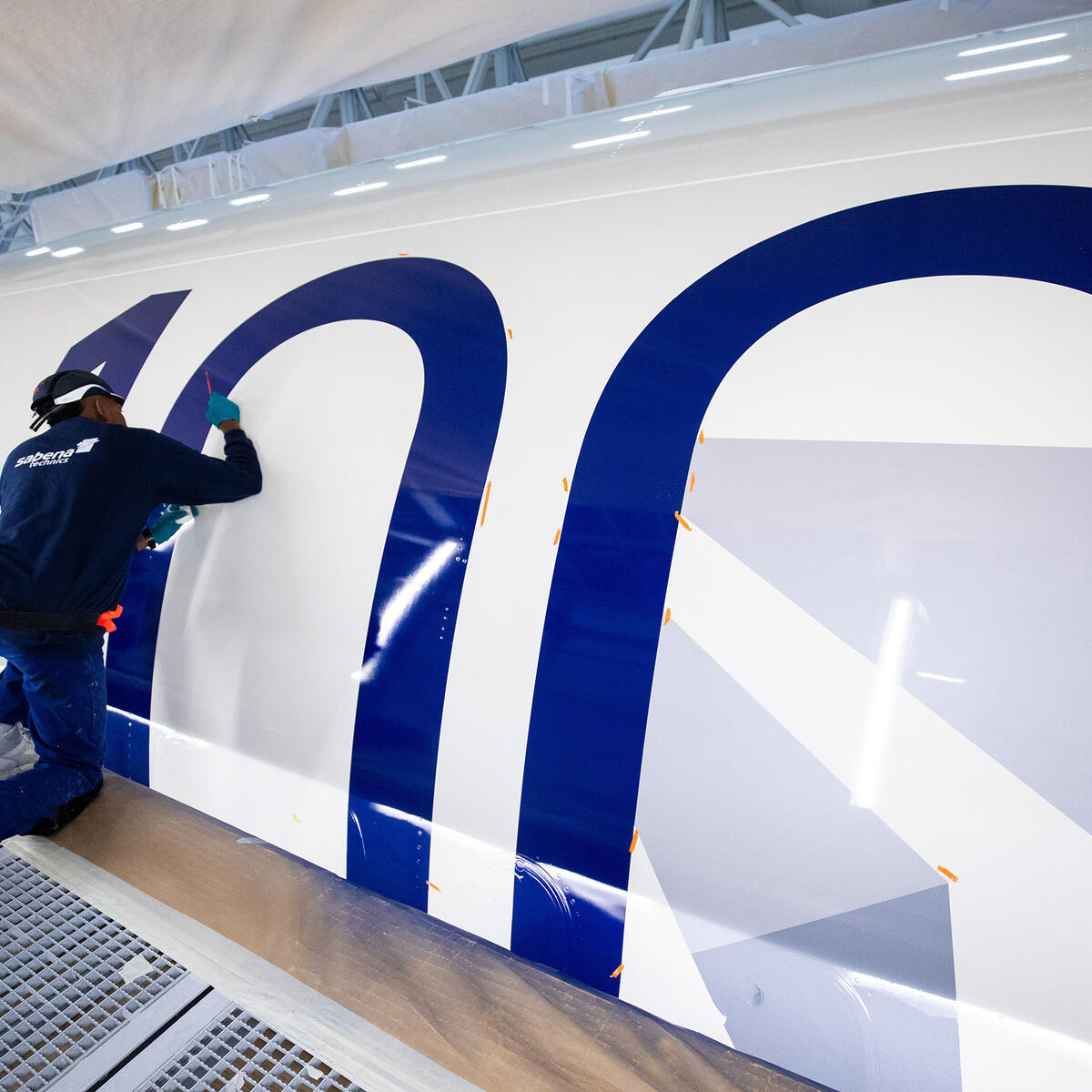 A bold 100 emblem is being painted on the side of a Delta aircraft.