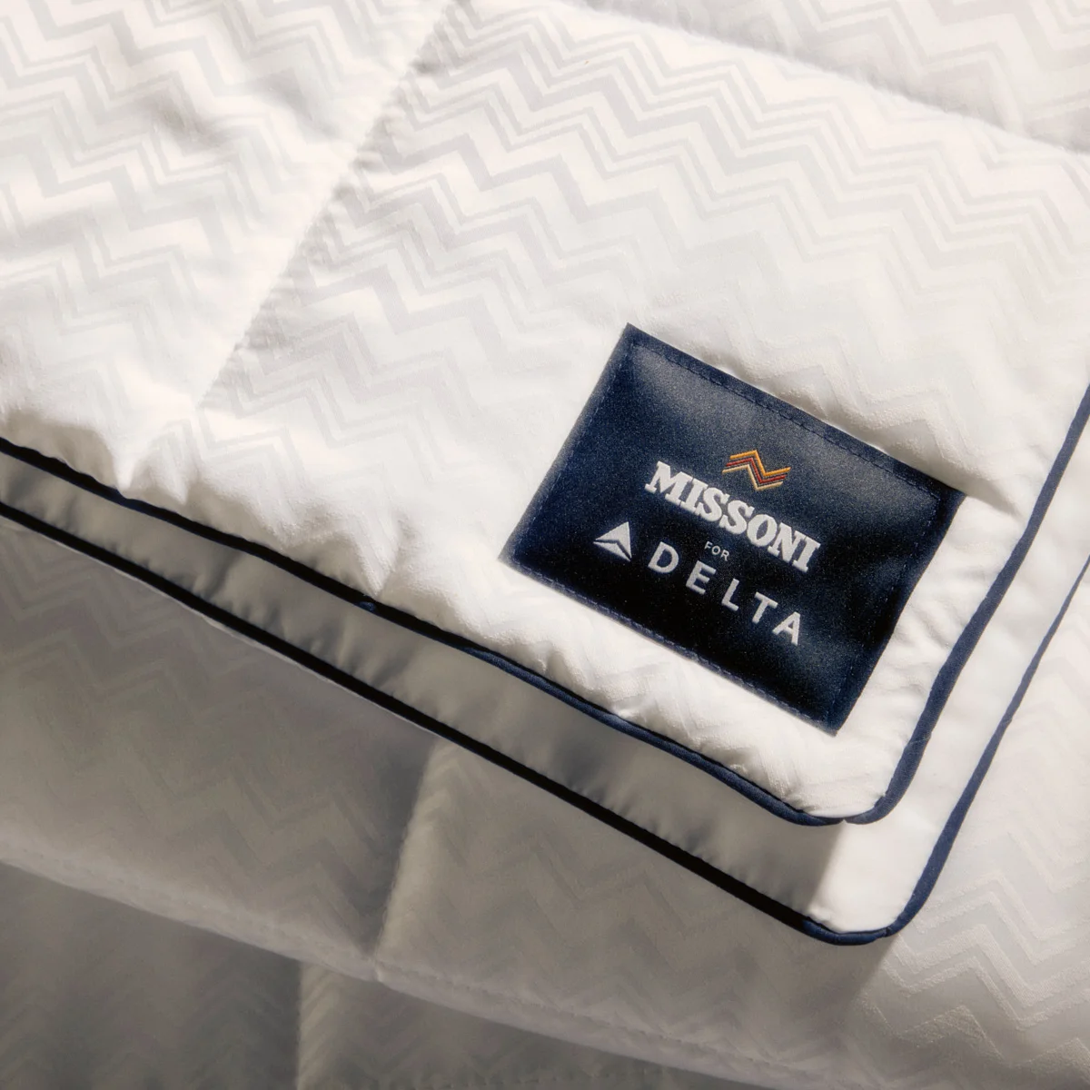 El nuevo juego de cama de Delta One incluye el edredón Missoni y una almohada blanca para dormir, con un sutil y elegante diseño en zigzag de Missoni y detalles en azul marino.