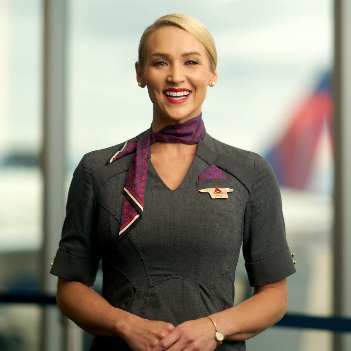 Delta flight attendant smiling, wearing gray dress and purple neck scarf.