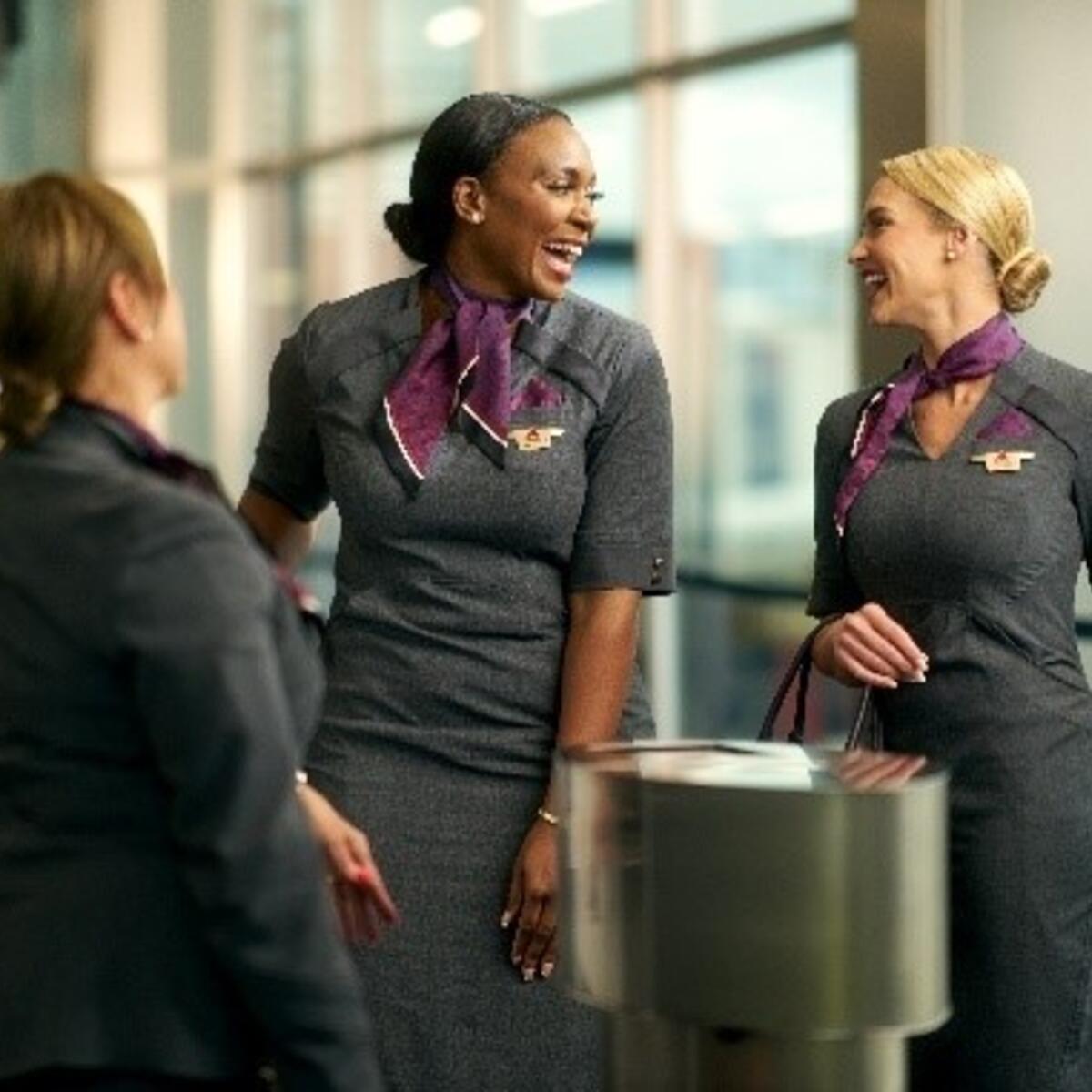 Three Delta flight attendants standing together, laughing with one another.