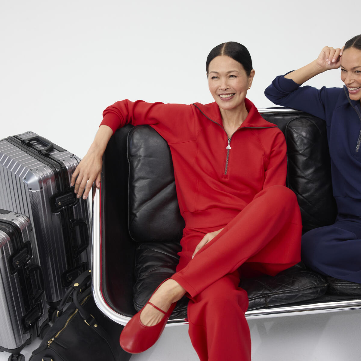 Two smiling women, sitting next to each other dressed in red and navy Spanx outfits.