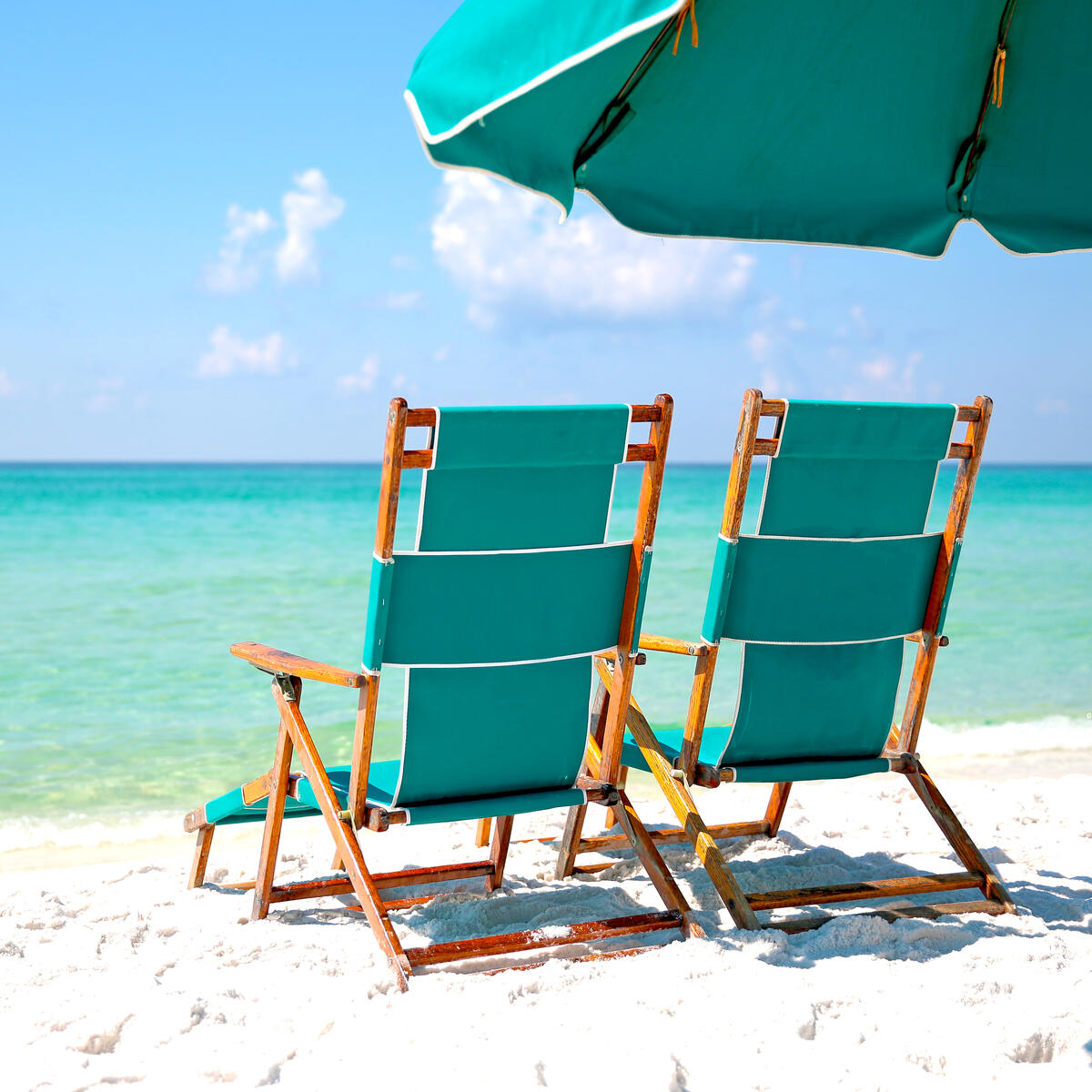 Two empty beach chairs in the sand facing turquoise blue ocean.