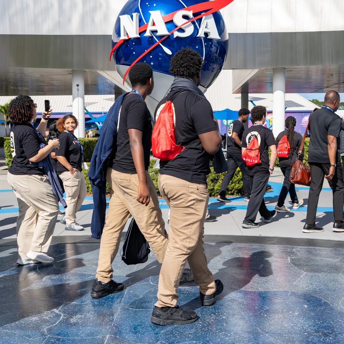 DREAM flight participants walking near a large NASA logo sculpture outdoors at the Kennedy Space Center.