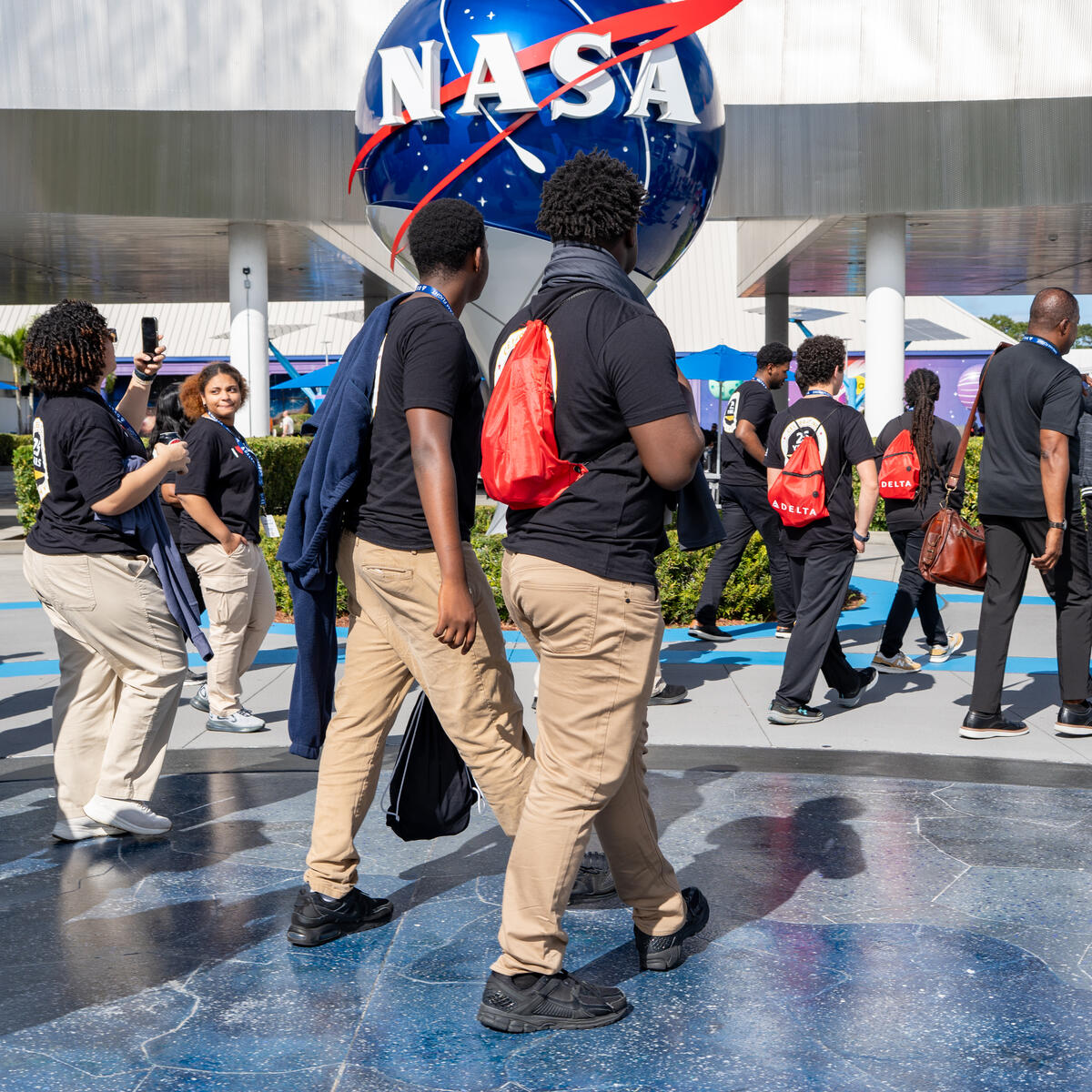 DREAM flight participants walking near a large NASA logo sculpture outdoors at the Kennedy Space Center.