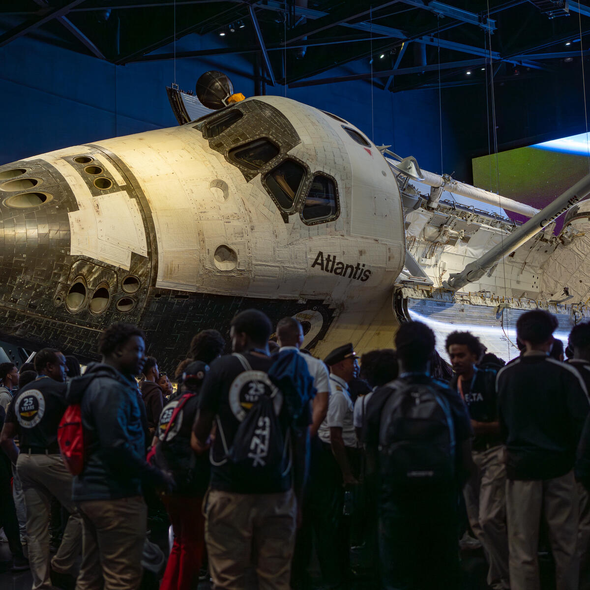 Space Shuttle Atlantis displayed in a museum exhibit with DREAM flight attendees gathered around.