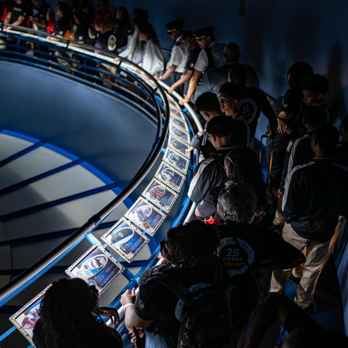 DREAM flight participants walking along a curved ramp lined with astronaut photos and memorabilia in a space-themed exhibit.