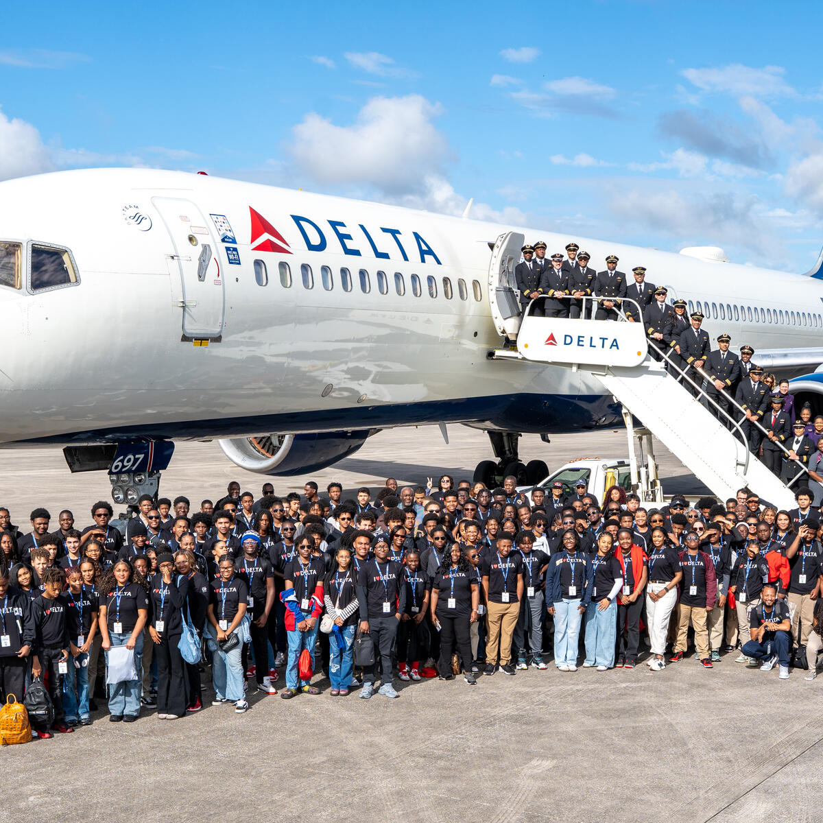 Group shot of DREAM flight attendees standing in front of Delta plane on tarmac. 