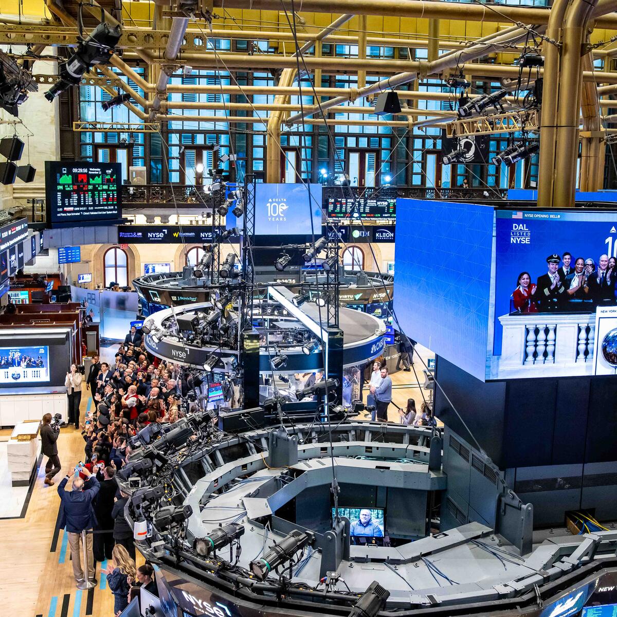 Overhead shot of NYSE floor with main screen displaying Ed and Delta people ringing the bell.