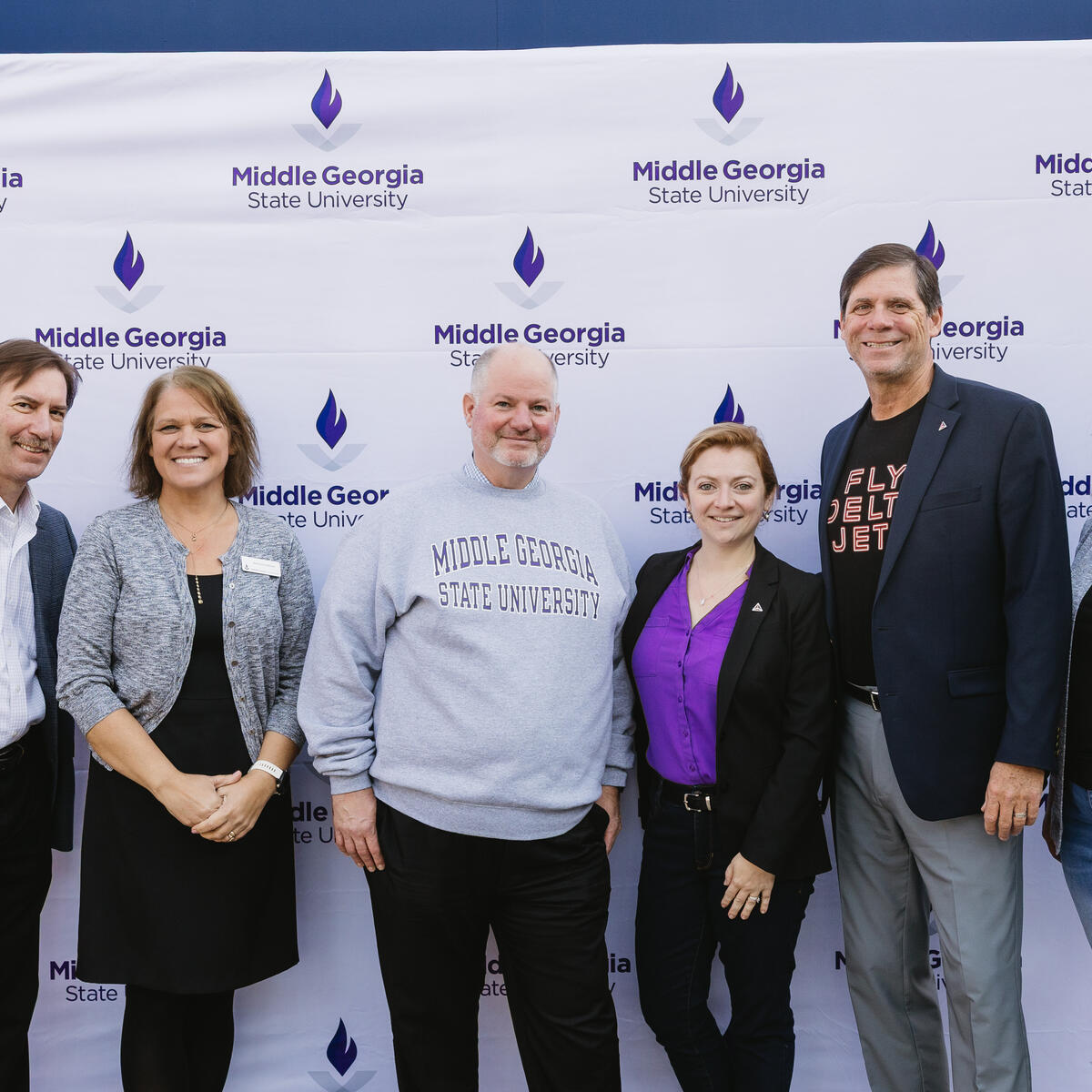 Six people standing in front of a Middle Georgia State University step-and-repeat banner, posing for a group photo.