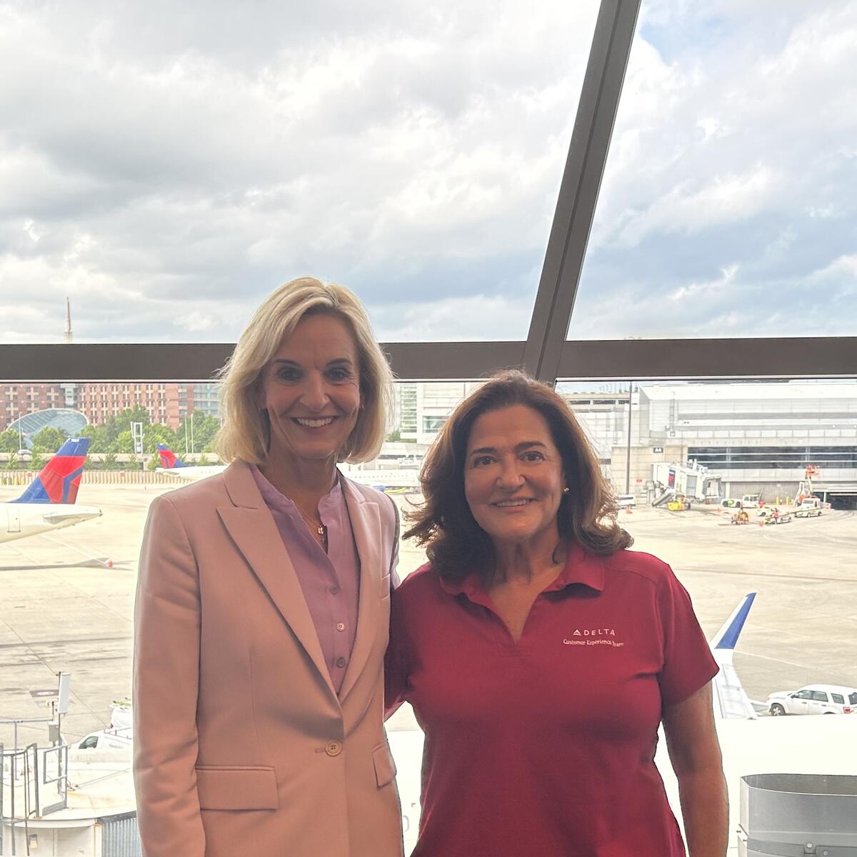 Delta employees Allison Ausband and Nancy Cohn posing against a backdrop of the Boston airport ramp.