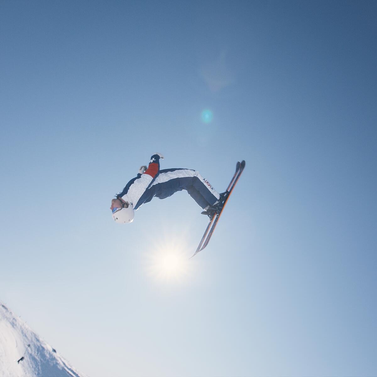 A skier performs a high aerial trick against a clear blue sky on a snowy mountain slope