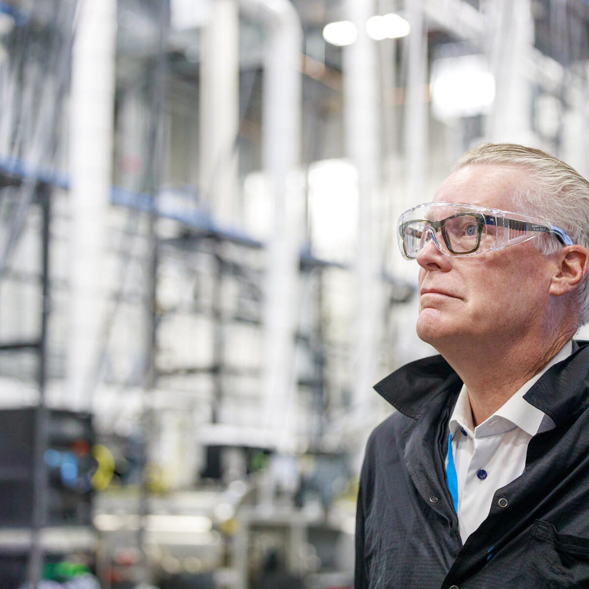 Ed Bastian wearing safety glasses standing inside an industrial facility with machinery and pipes in the background.