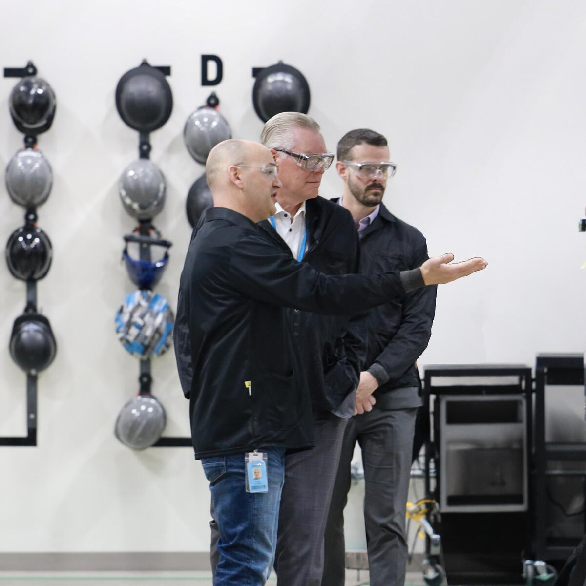 Three people wearing safety glasses review equipment inside an industrial facility.