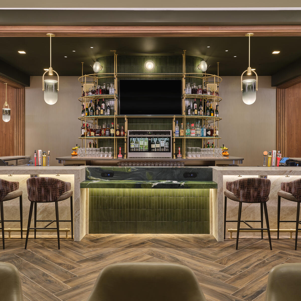 Front view of lounge bar with high‑back stools, illuminated shelving, pendant lights and wood‑pattern flooring