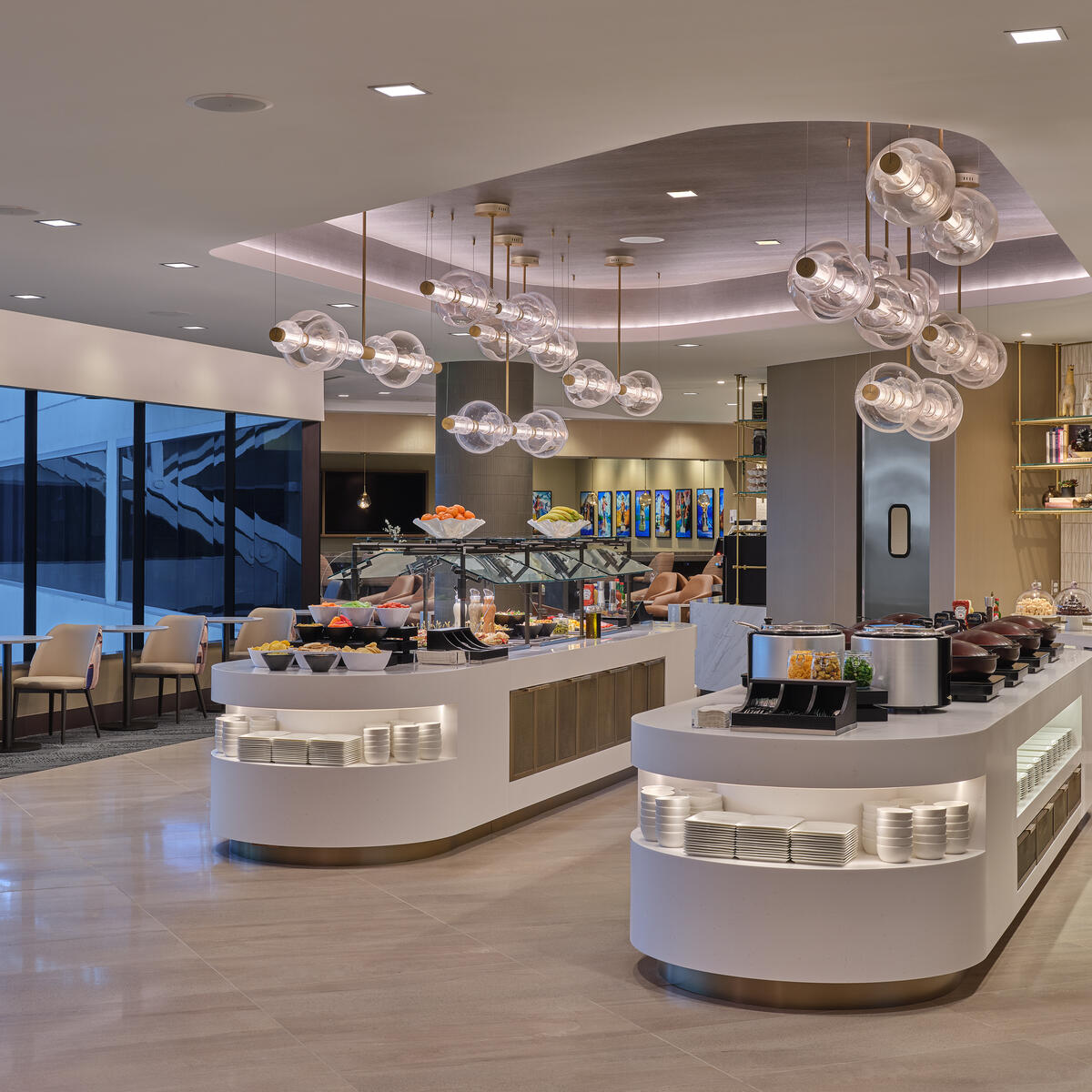 Modern buffet area with curved food stations, hanging globe lights and seating along large windows