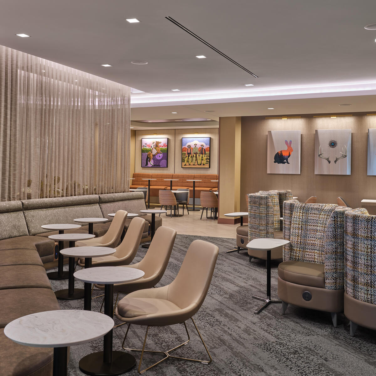 Central lounge area with cushioned seating, small round tables, soft divider curtains and colorful artwork on the walls