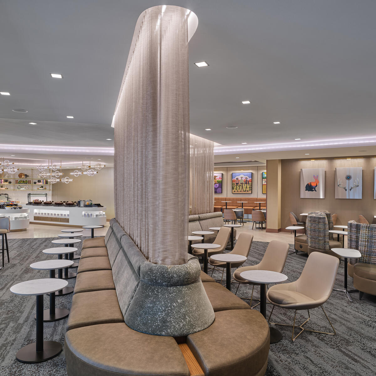 Spacious central area of lounge with curved privacy dividers, varied seating areas, small round tables and a buffet area in the background