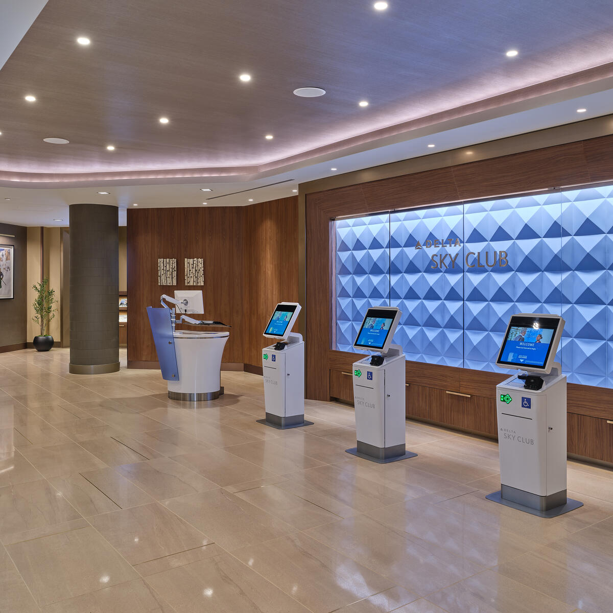 Denver Sky Club entrance with self‑service kiosks, a textured blue wall behind the Sky Club sign and a reception desk in a spacious, well‑lit lobby