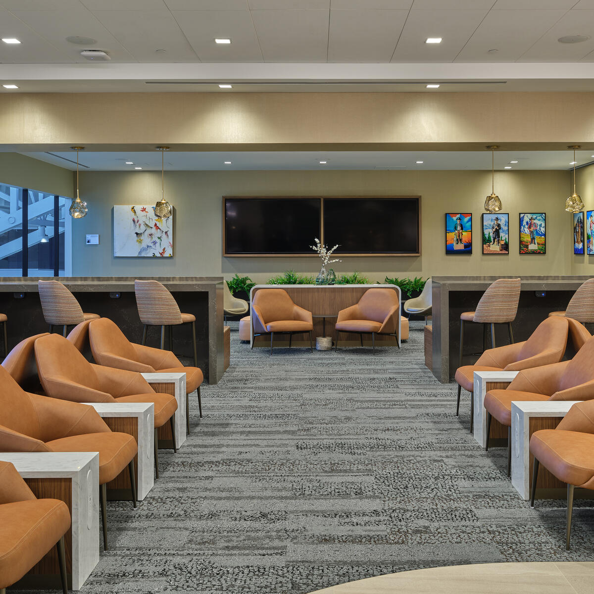 North lounge area with rows of tan lounge chairs, bar‑height seating, modern lighting and colorful artwork on the walls
