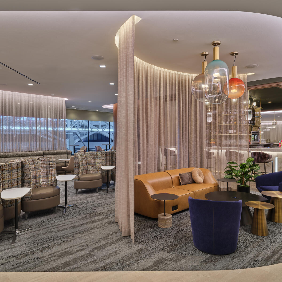 West lounge area with curved seating, soft lighting, privacy curtains and a bar with colorful hanging lights