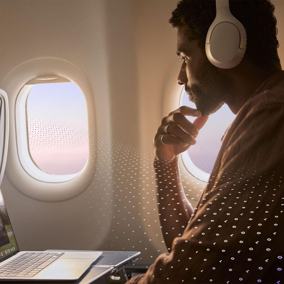A passenger seated by an airplane window uses a laptop and wears over‑ear headphones, with an in‑flight entertainment screen visible and a subtle digital pattern overlay.
