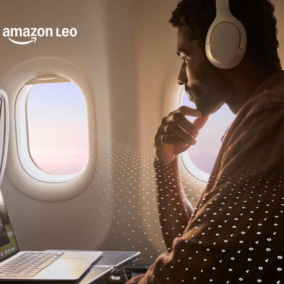  A customer seated by an airplane window uses a laptop and wears over‑ear headphones, with an in‑flight entertainment screen visible and a subtle digital pattern overlay.