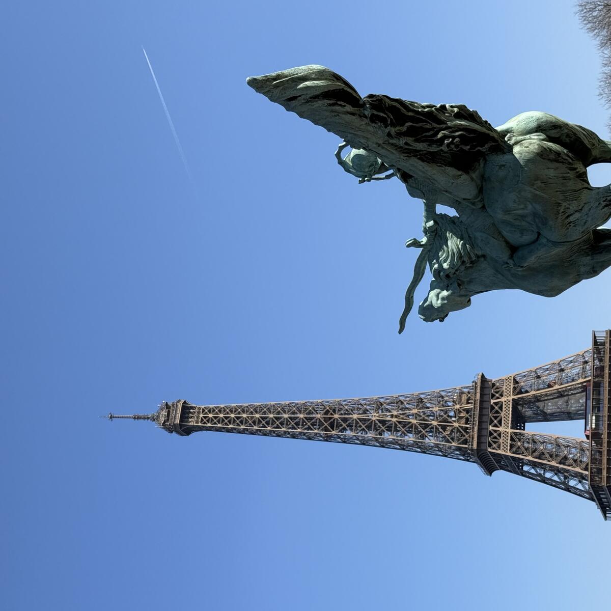 A bronze statue of the winged horse Pegasus is in the foreground, with the Eiffel Tower prominent in the background under a blue sky, viewed from the Pont de Bir-Hakeim.
