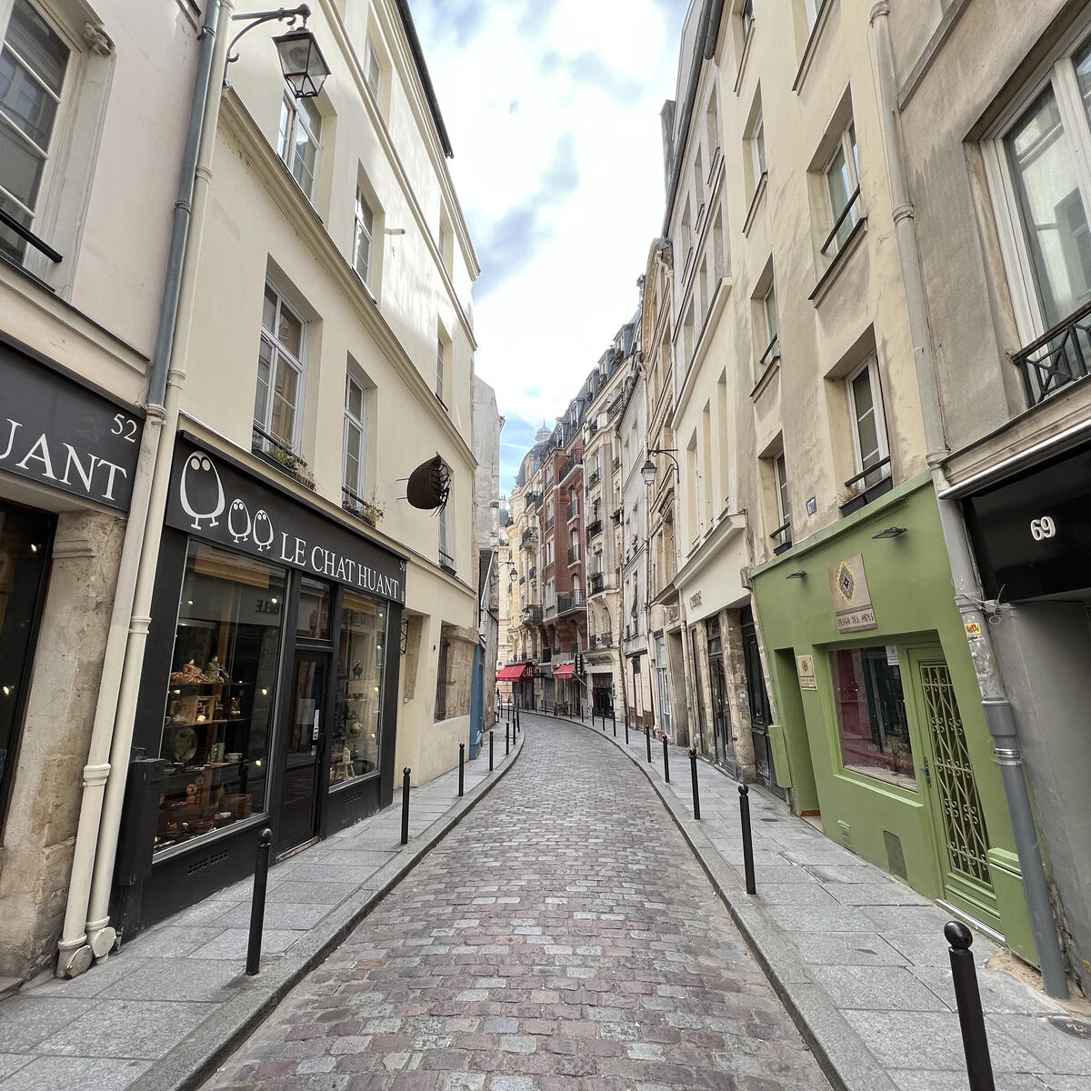 Narrow cobblestone street lined with small boutiques and pastel buildings in a historic Paris neighborhood.