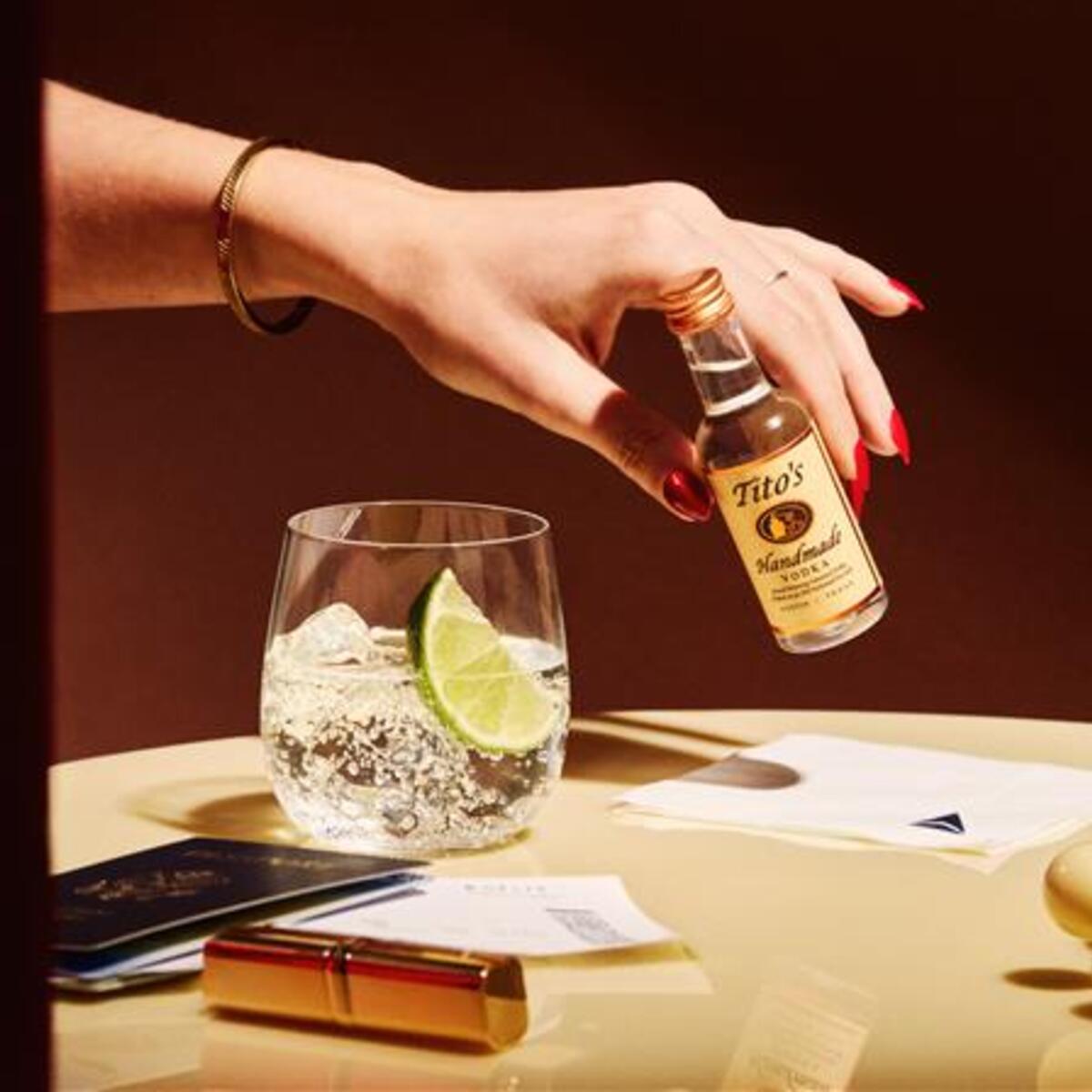 A hand holds an airplane bottle of Tito's Vodka