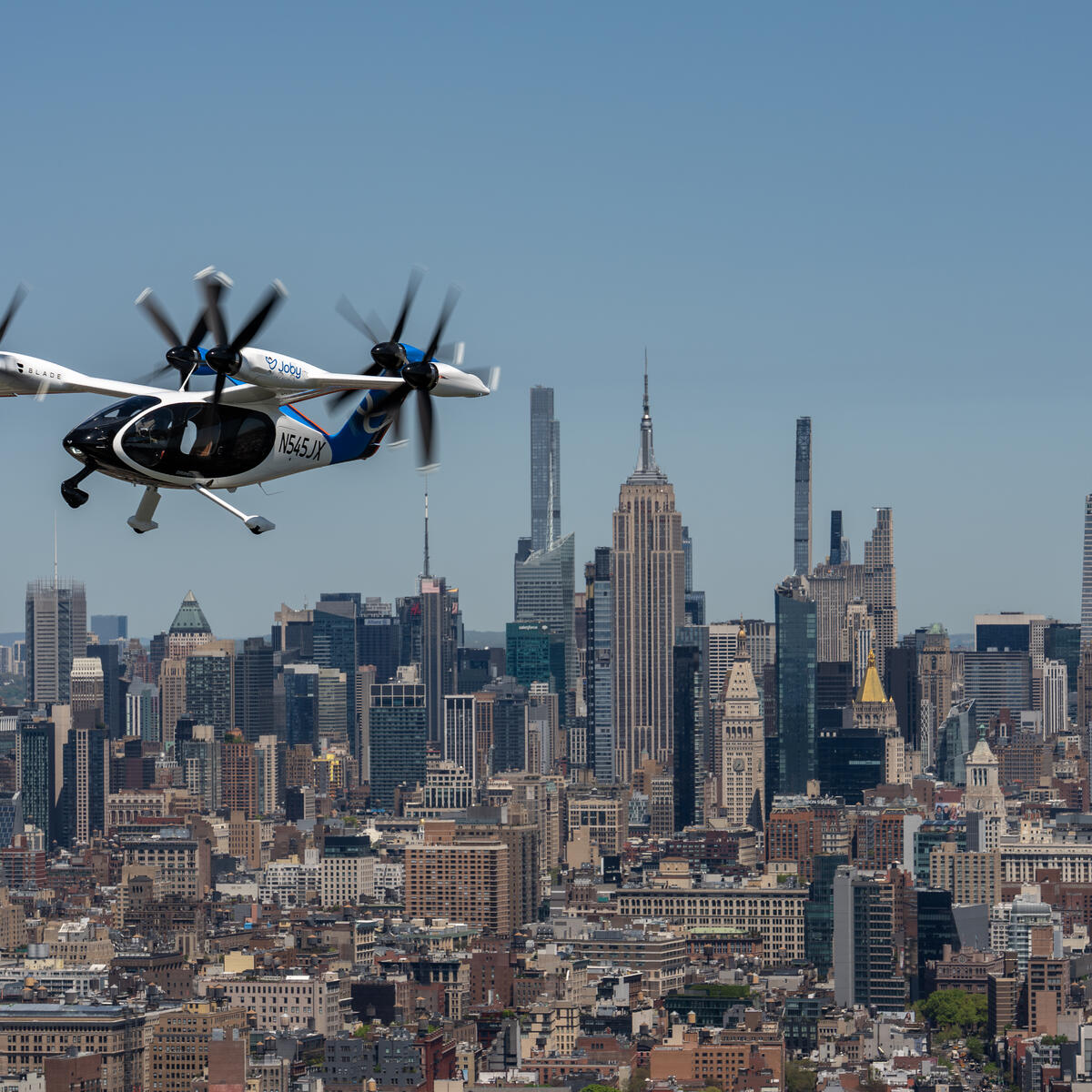 Joby electric air taxi flying above midtown Manhattan with the city skyline below.