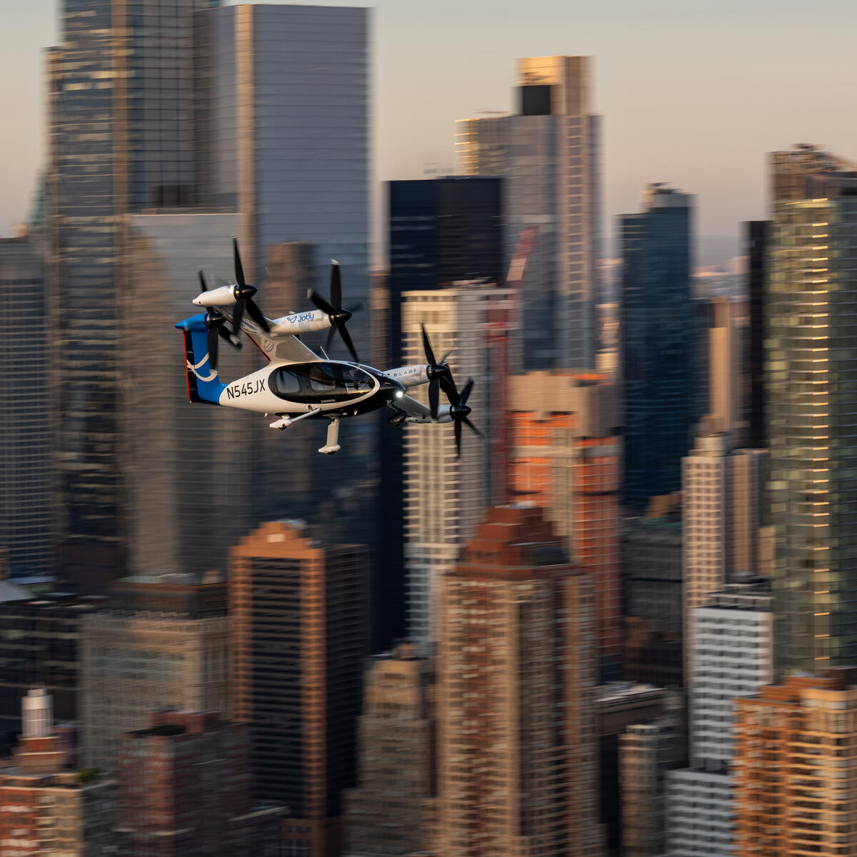 Joby Electric air taxi flying above midtown Manhattan with blurry city skyline in the background.