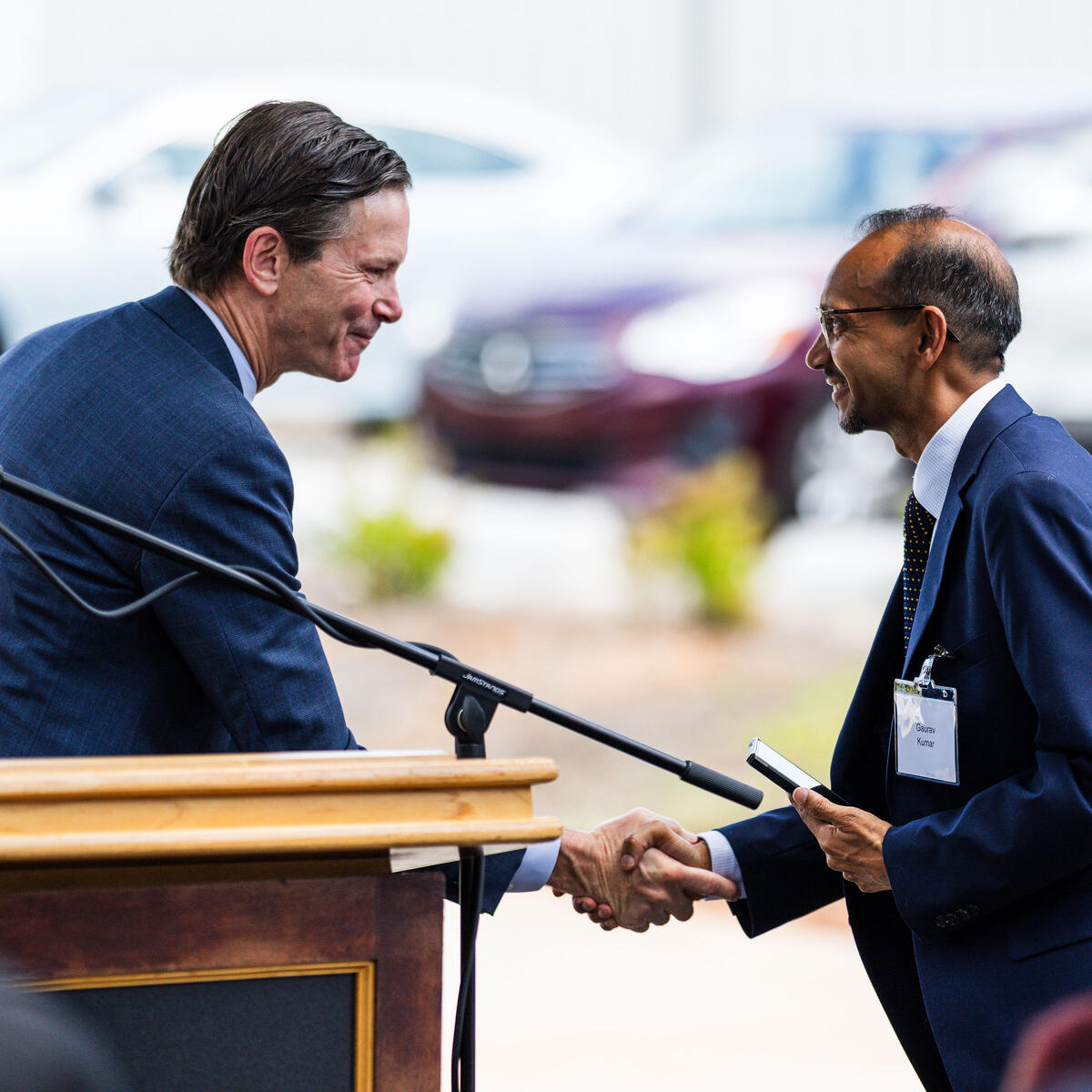 Two individuals exchange a handshake near a podium and microphone at an event