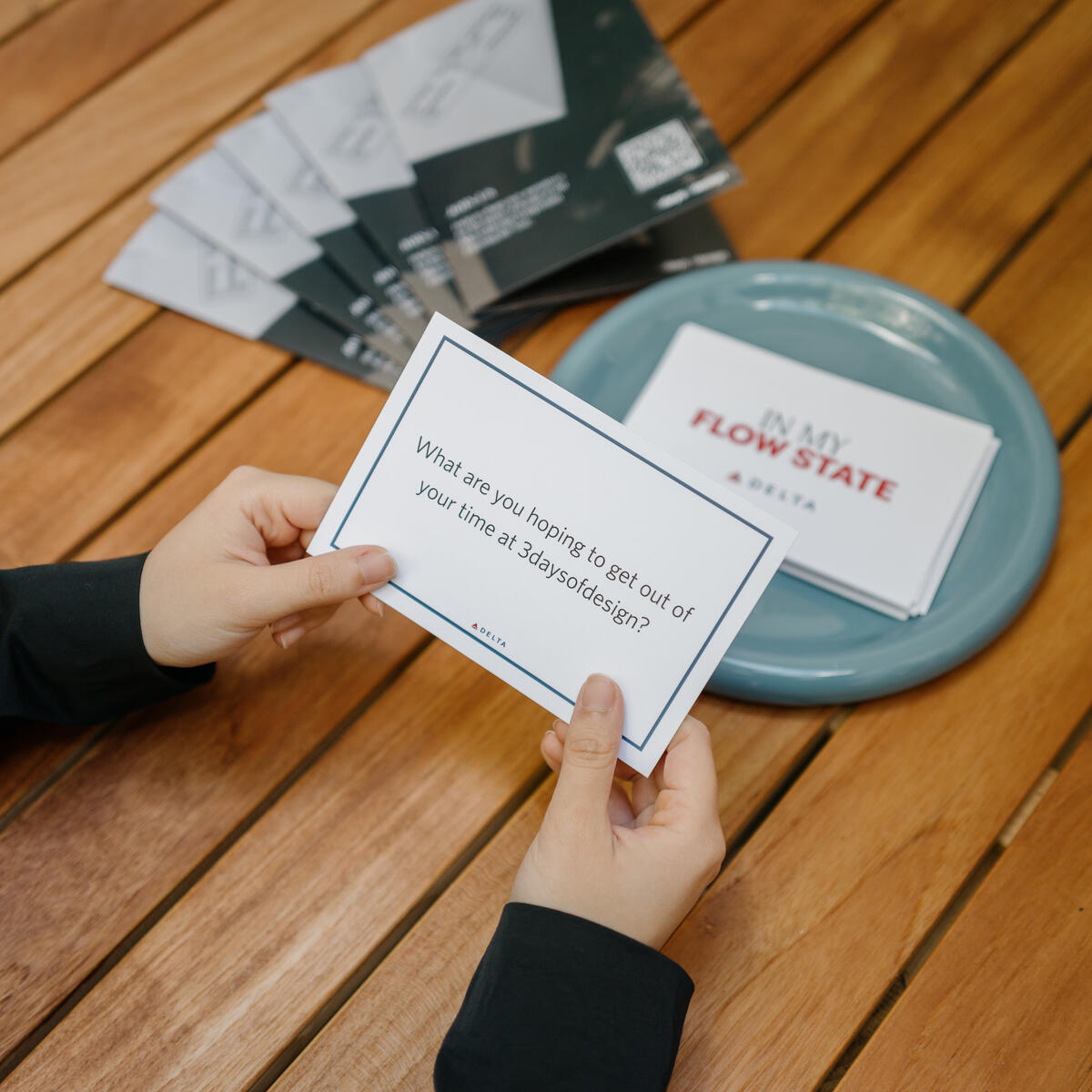 Hands holding a prompt card over a wooden table beside a bowl of cards, reading “What are you hoping to get out of your time at 3daysofdesign?”