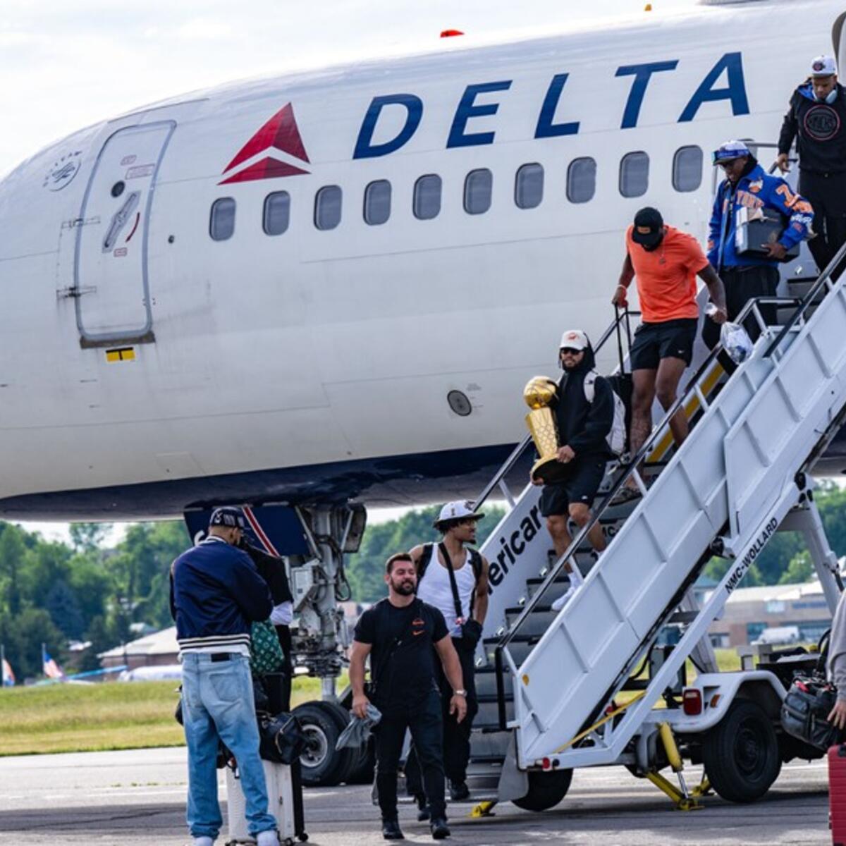 People exit a Delta airplane via stairs on the tarmac, with one person carrying a gold trophy while others hold bags nearby.