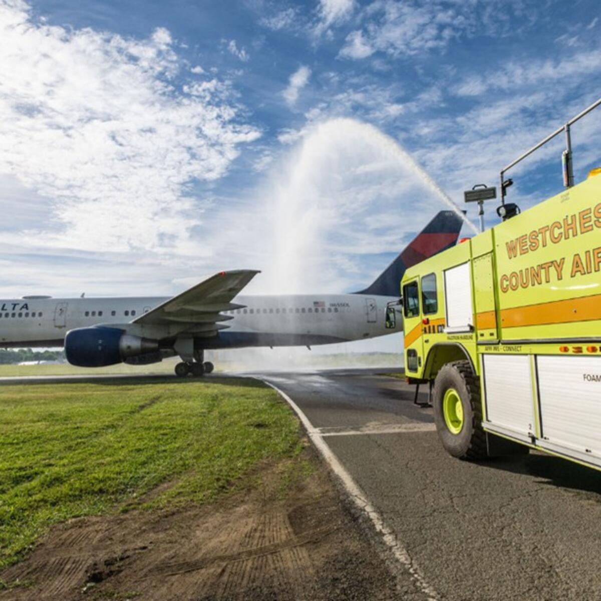 Delta airplane receives water salute from airport fire truck on runway.