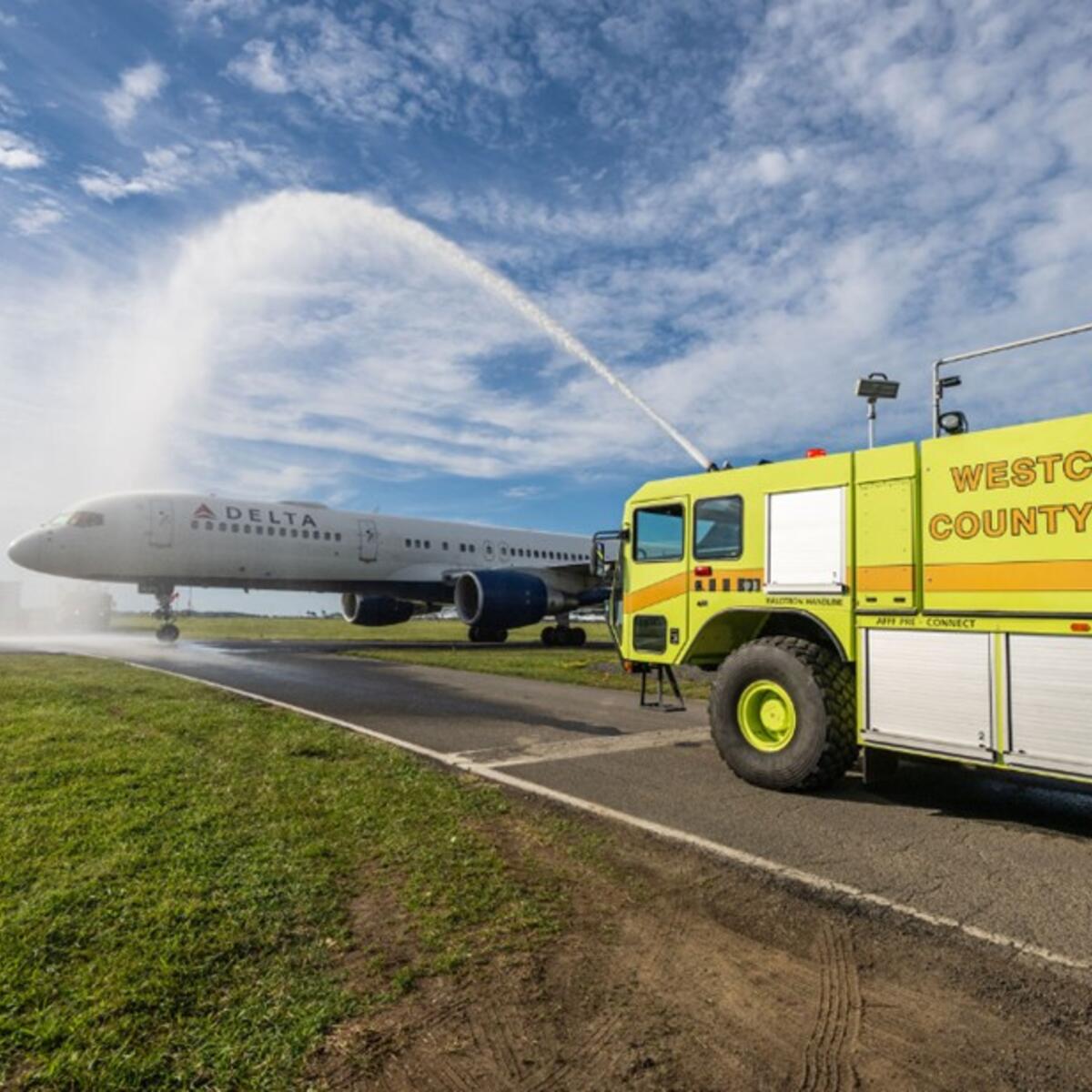 Delta airplane receives water salute from airport fire truck on runway.