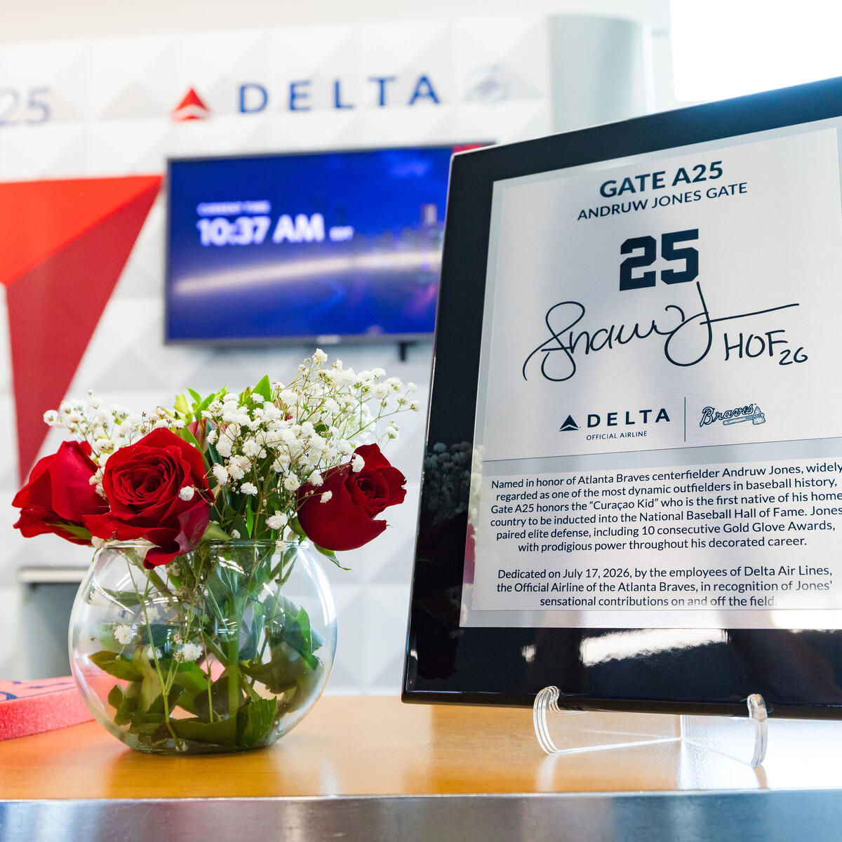 Commemorative plaque honoring Andruw Jones at Delta Gate A25 displayed beside a vase of red roses, with Delta branding visible in the background.