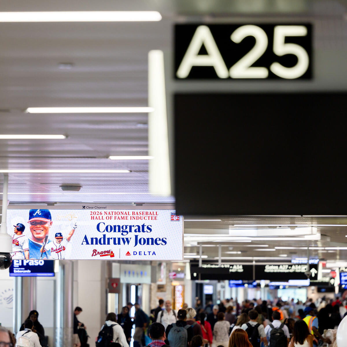 Crowded airport concourse near Gate A25, with a digital sign congratulating Andruw Jones on his National Baseball Hall of Fame induction and Delta branding visible throughout the terminal.