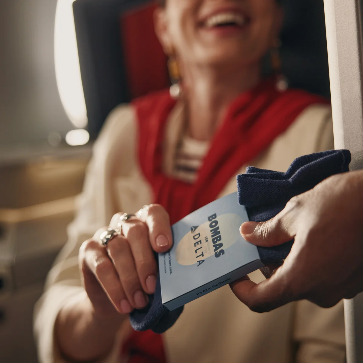 Customer receives a pair of Bombas socks while seated in a Delta One suite.